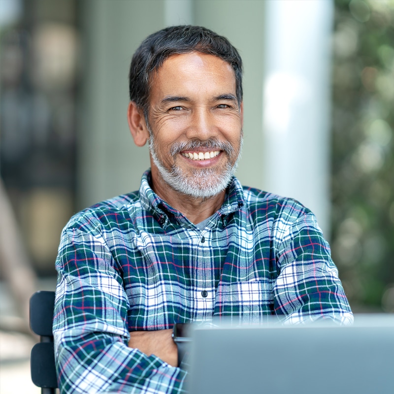 Un hombre con pelo y barba gris, sonríe confiado con un portátil de soluciones capital.